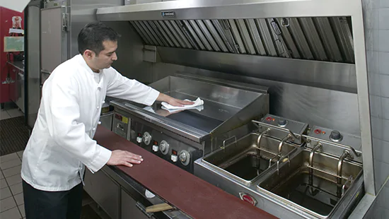 A man degreasing a commercial grill with Blue Bomber